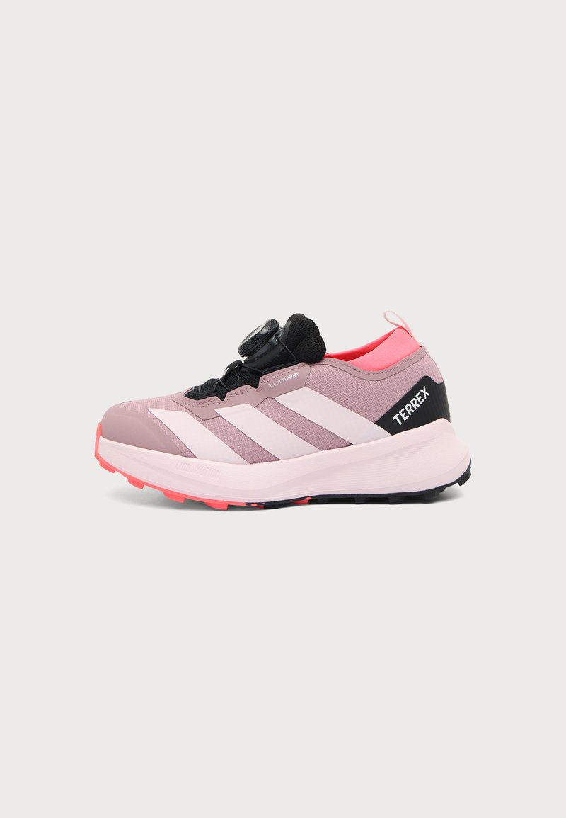 Ροζ ανοιχτό και μαύρο sneaker Adidas Terrex με λευκές ρίγες και σύστημα κλεισίματος με διακόπτη, σχεδιασμένο για υπαίθριες δραστηριότητες, εμφανίζεται από το πλάι.