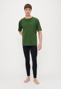 Πράσινο κοντομάνικο πουκάμισο με μανίκια ράγκλαν, συνδυασμένο με μαύρο εφαρμοστό κολάν. Το πουκάμισο διαθέτει μικρό λογότυπο στο στήθος. Ομαλή υφή.