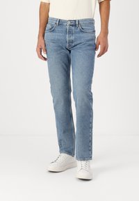Jeans en denim bleu clair avec une coupe droite, un design à cinq poches et une fermeture à bouton. Assortis à des baskets blanches.