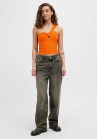 Top corto de punto naranja con detalle de ojal, combinado con jeans gris desgastado de corte holgado y botas negras. Tejido texturizado y una tirante en el hombro.