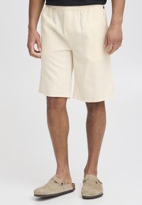 Shorts jaune clair avec un motif texturé, taille élastique et poches latérales, associés à des chaussures beige en daim à enfiler.