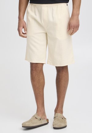 Light yellow shorts with a textured pattern, elastic waistband, and side pockets, paired with beige suede slip-on shoes.