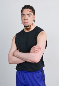 Fekete ujjatlan póló kék sportnadrággal. A póló egyszerű dizájnnal rendelkezik, a nadrágon pedig fekete oldalsávok találhatóak.