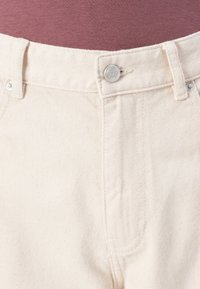 Pantalones de mezclilla beige con una superficie texturizada, con cierre de botón en la parte frontal, trabillas para cinturón y diseño recto.