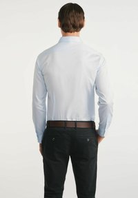 Jasnoniebieska koszula z długim rękawem z klasycznym kołnierzykiem, gładką tkaniną i zapięciem na guziki przy mankietach. Zestawiona z ciemnymi spodniami i brązowym paskiem.