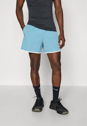 Lyseblå badebukser med hvid kant, lavet af letvægtsstof, har en elastisk talje og en afslappet pasform. Bæres med en sort tanktop.