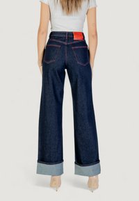 Jeans de mezclilla oscuros de pierna ancha con puños enrollados en azul claro, costuras contrastantes en rojo y una etiqueta de cuero en la parte posterior. Diseño de cinco bolsillos.