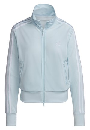 Survêtement Adidas bleu clair avec des rayures blanches sur les manches et le pantalon, veste à fermeture éclair frontale, poches latérales zippées, mains dans les poches.