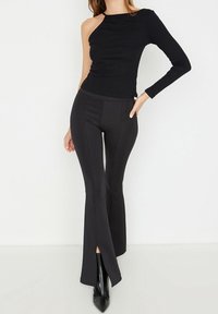 Svart enaxlad topp med lång ärm, matchad med tajta svarta utsvängda byxor. Slät tyg med subtil lyster och vertikala sömdetaljer.