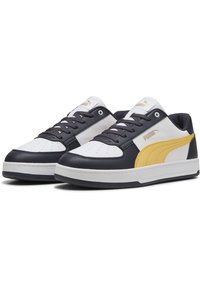 Hvide og marineblå lædersneakers med et gult accent. Har perforeret tåboks, runde snørebånd og en kraftig hvid sål. Puma-logoet er vist.