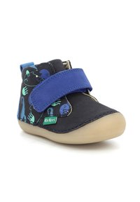 Schwarzer Stoffschuh mit blauer Klettverschluss, Cartoonmuster in Grün und Blau, abgerundete Zehenpartie und beiger Gummisohle. Kickers-Logo sichtbar.