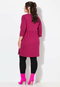 Vestido fucsia hasta la rodilla con mangas tres cuartos, cintura fruncida, combinado con leggings negros ybotas de tobillo fucsias.