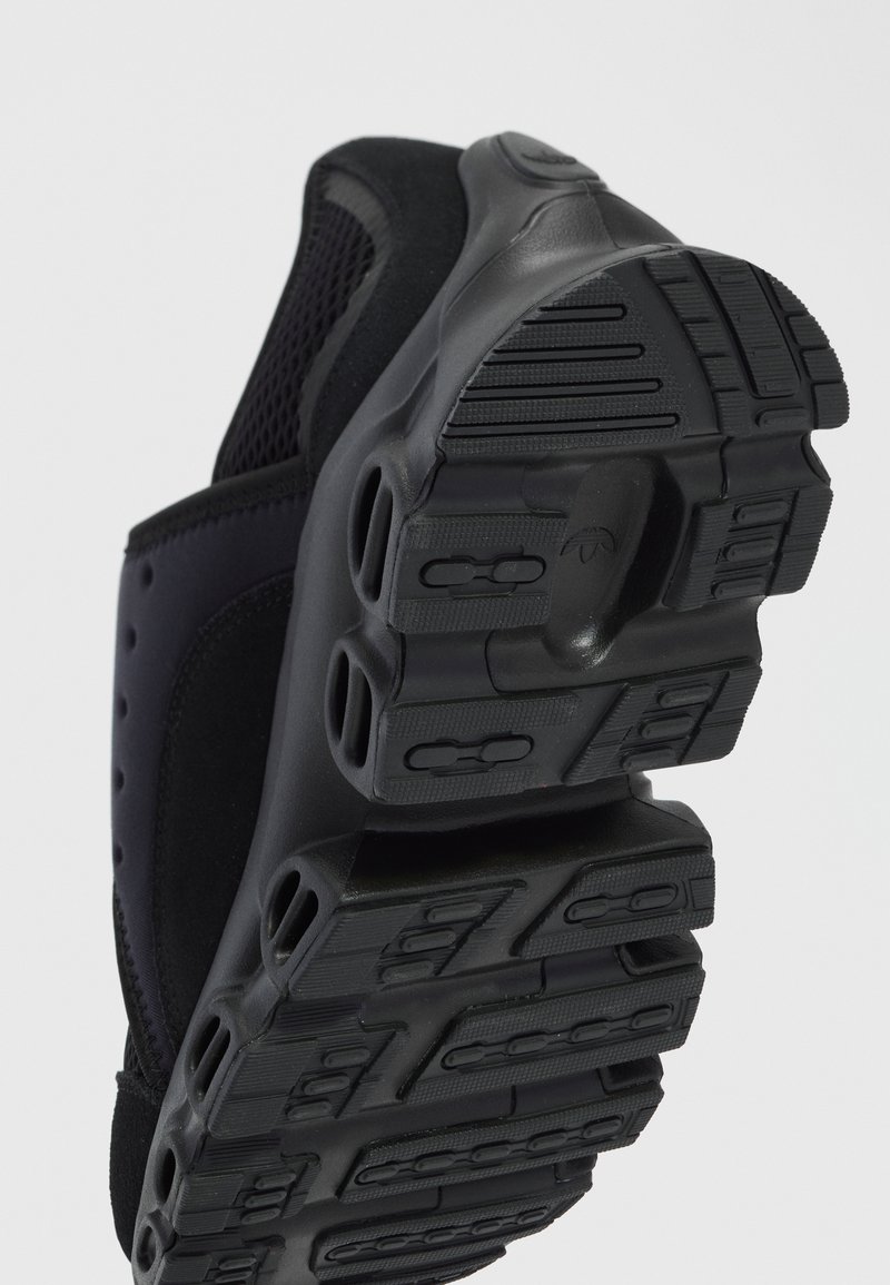 Chaussure de sport noire, avec une semelle en caoutchouc texturé avec des rainures, un dessus en mesh et des accents synthétiques lisses pour un soutien et une respirabilité accrus.