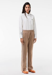 White button-up shirt, brown patterned trousers with blue and white stripes, and orange sneakers. Smooth fabric with a relaxed fit.