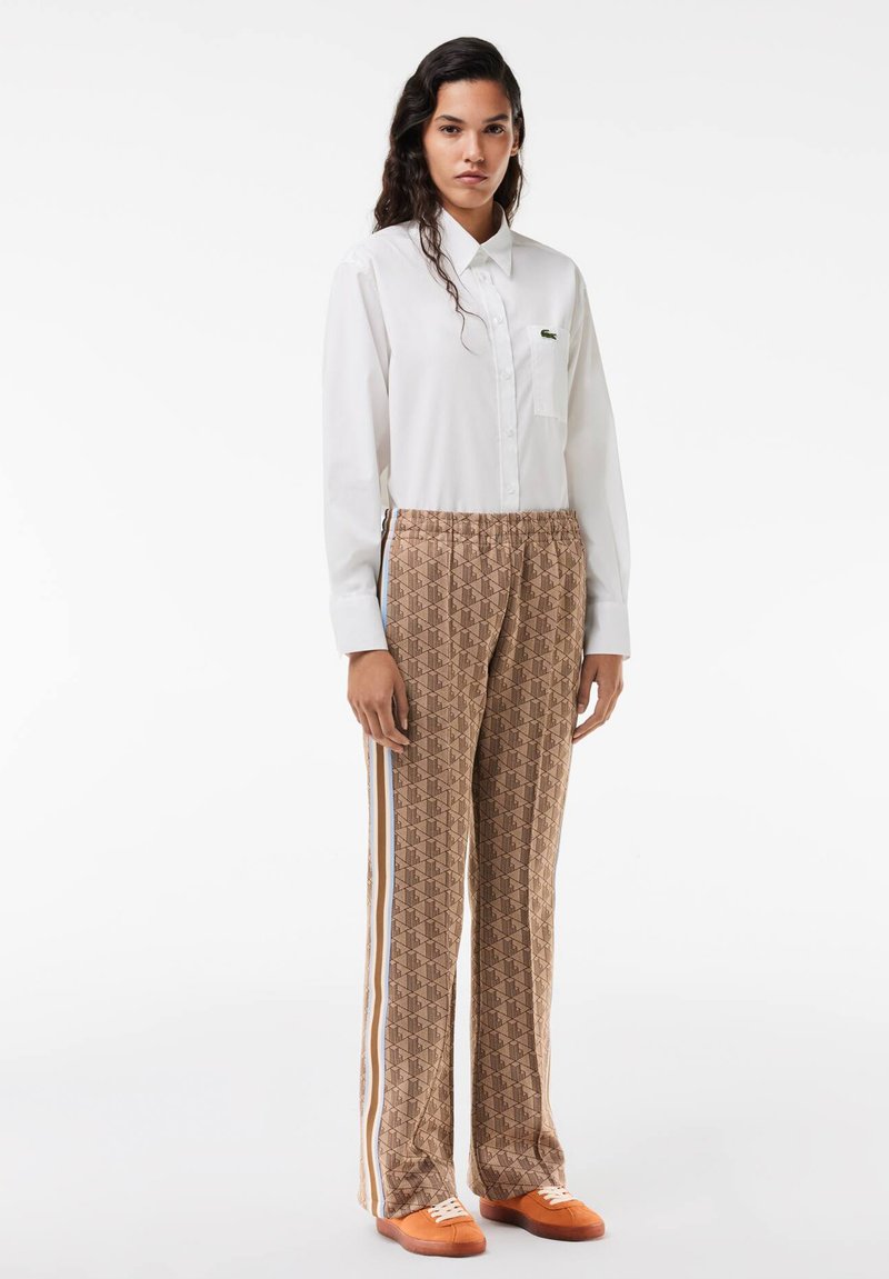 Biała koszula z guzikiem, brązowe spodnie w deseń z niebieskimi i białymi paskami oraz pomarańczowe sneakersy. Gładki materiał o luźnym kroju.