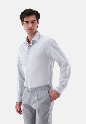 Hellgraues Langarmshirt mit spitzem Kragen und Knopfleiste, kombiniert mit grauen, taillierten Hosen mit seitlichen Verstellungen.