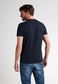 T-shirt di cotone blu scuro con maniche corte, scollatura rotonda e una texture liscia. Indossato con jeans in denim azzurro.