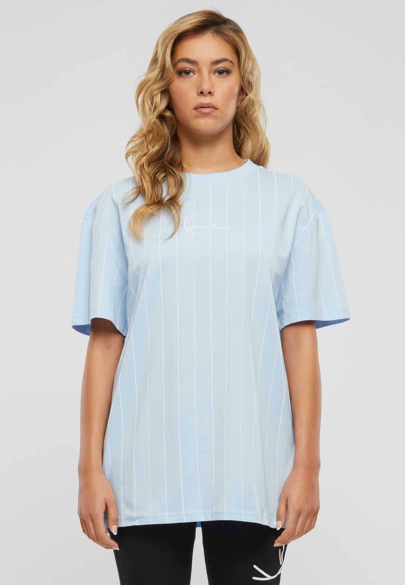 Helles blaues übergroßes T-Shirt mit weißen vertikalen Streifen und einem Rundhalsausschnitt. Beinhaltet ein kleines Logo im Brustbereich.