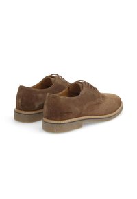 Chaussures en suede marron avec une finition lisse, dotées de bouts ronds, d'un laçage et de semelles en caoutchouc texturé. Marquage discret sur le côté.