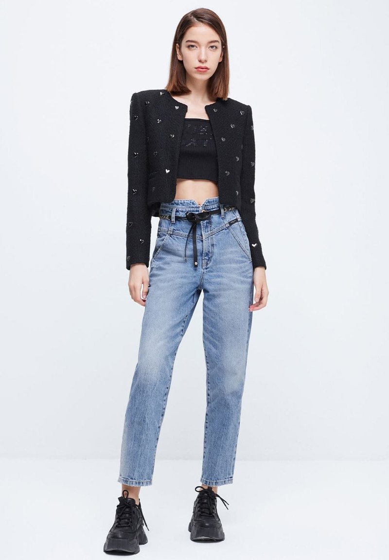 Chaqueta negra corta con acentos de corazón, combinada con jeans de tiro alto en tono azul claro. El modelo lleva zapatillas negras con un acabado texturizado.