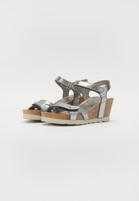 Silberne Keilsandalen mit Kreuzriemen, einem korkähnlichen Absatz, offener Zehenpartie und Gummisohle. Texturierte metallische Oberfläche.