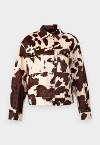 Jeansjacka med nötkreaturstryck som har en beige bakgrund med bruna fläckar, spetsig krage och silverfärgade knappstängningar fram och i fickorna.