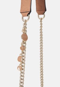 Kožený pásek v béžové barvě s černými okraji, zdobený zlatými řetězy a kulatými kovovými detaily s ražbou "GUESS" a "EST 1981".