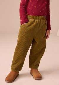 Olivengroene corduroy broek met een losse pasvorm, diepe zakken en een elastische tailleband. Gecombineerd met bruine suède enkellaarsjes.