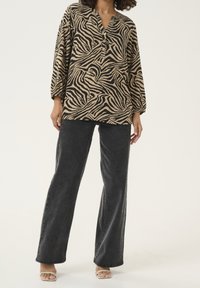 Blouse à imprimé animalier beige et noir, dotée d'un col en V et de boutons. Associée à un jean large gris foncé et des sandales beige tanné.