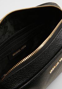 Vnitřek černé kožené tašky s texturovaným povrchem, zlatým zipem a hladkým podšívkou. Obsahuje více přihrádek a značkovou etiketu.