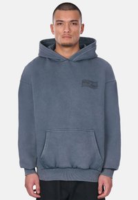 Grauer Kapuzenpulli mit einer Kängurutasche, gerippten Bündchen und Saum sowie einem kleinen, aufgedruckten Logo auf der linken Brust.