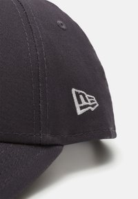 Casquette de baseball gris foncé en tissu texturé, avec un logo brodé blanc sur le côté et des détails de couture visibles.