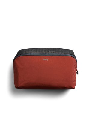 Bustina da viaggio rettangolare compatta in tessuto arancione ruggine con parte superiore in rete nera e cerniera, marchiata "bellroy" al centro anteriore.