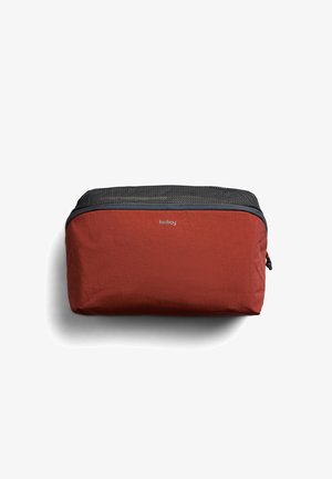 Pochette de voyage rectangulaire compacte en tissu orange rouille avec dessus en mesh noir et fermeture éclair, marquée "bellroy" au centre sur le devant.