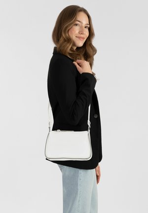 Sac à main en cuir blanc avec une finition lisse, doté d'une bordure argentée et d'une bandoulière amovible, présenté par un mannequin portant un blazer noir.