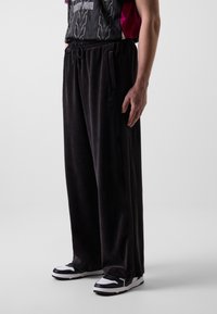Nederdele i sort velour med elastisk talje og snøre, og med sidelommer. Kombinationen er med sorte og hvide sneakers.