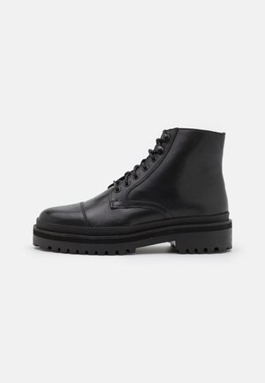 Black leather ankle boots feature a rounded toe, lace-up design, and a sturdy rubber sole with a textured tread pattern.