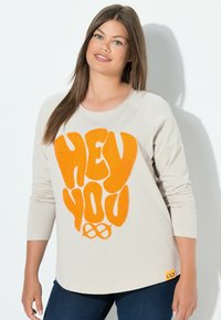 Beige långärmad skjorta med iögonfallande orange "HEY YOU" text i en strukturerad design. Tillverkad av bomull med avslappnad passform och rund halsringning.