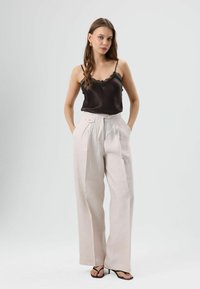 Zwarte zijden cami met kanten rand, gecombineerd met lichtbeige wijde broek met voorplooien en twee knopen. Zwarte sandalen maken de look af.