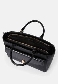 Svart skinn tote-veske med glatte og teksturerte aksenter, med glidelås på toppen, to håndtak og innvendige rom. Detaljer i gullhardware.