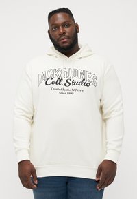 Cremefarbener Hoodie mit großen schwarzen Buchstaben "JACK & JONES Coll. Studio" auf der Vorderseite, ausgestattet mit einer Kapuze mit Kordelzug sowie gerippten Bündchen und Saum.