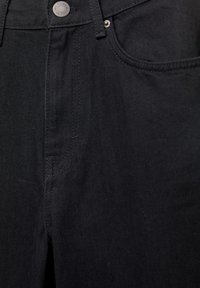 Jean en denim noir avec une texture lisse, doté d'une fermeture avant à boutons et zip, deux poches et des détails de couture subtils.