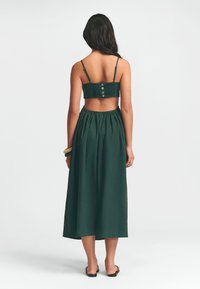 Groene tweedelige jurk met een smocked crop top met knopen op de rug en een vloeiende maxi rok, gemaakt van lichte stof.