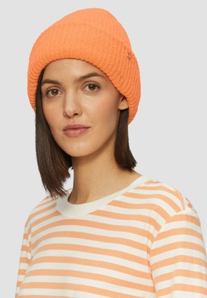 Oranje geribde beanie met een zachte textuur, voorzien van een kleine metalen accent, gecombineerd met een crèmekleurig gestreept shirt.