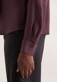 Langarmhemd aus Pflaumenstoff, mit einem geknöpften Bund und einer glatten Textur, kombiniert mit maßgeschneiderten schwarzen Hosen.