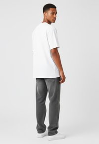 T-shirt bianco a maniche corte, vestibilità rilassata, abbinato a jeans grigi con una leggera texture e sneakers bianche. Modello rivolto di spalle rispetto alla fotocamera.