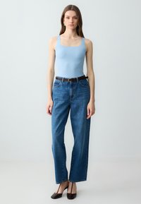 Body blu chiaro senza maniche, jeans blu a vita alta, cintura marrone e sabot marroni scuri con tacco. Silhouette semplice e strutturata.