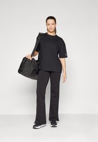 Svart oversized t-skjorte, vide svarte bukser og en svart gymbag. Antrekket har et enkelt design med en avslappet passform og uten mønstre.