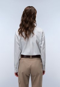 Back view of a long-sleeved, light blue and white striped shirt, made of cotton, paired with khaki pants and a dark brown belt.