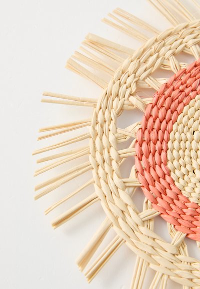 Rundvevd bordmatte laget av naturlige fibre i beige og rosa toner, med et teksturert sirkulært mønster og frynsete kanter.